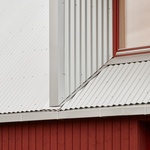 Budova se skládá z lineárního objemu dřevěných panelů, obklopených v přízemí červenými dřevěnými prkny a kovovou trojúhelníkovou střechou z vlnité oceli. Foto: Madara Kuplā Budova se skládá z lineárního objemu dřevěných panelů, obklopených v přízemí červenými dřevěnými prkny a kovovou trojúhelníkovou střechou z vlnité oceli. Foto: Madara Kuplā