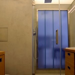 Původní samostatná koupelna a WC byly spojeny do jedné místnosti. Stěny i podlaha jsou opatřeny betonovou stěrkou a sprcha má namísto vaničky vyzděný sokl, ve kterém je umístěn odtokový žlábek. V pozadí je vidět ocelový rám se skleněnými tvárnicemi (profilit, copilit) umožňující prosvětlení koupelny denním světlem